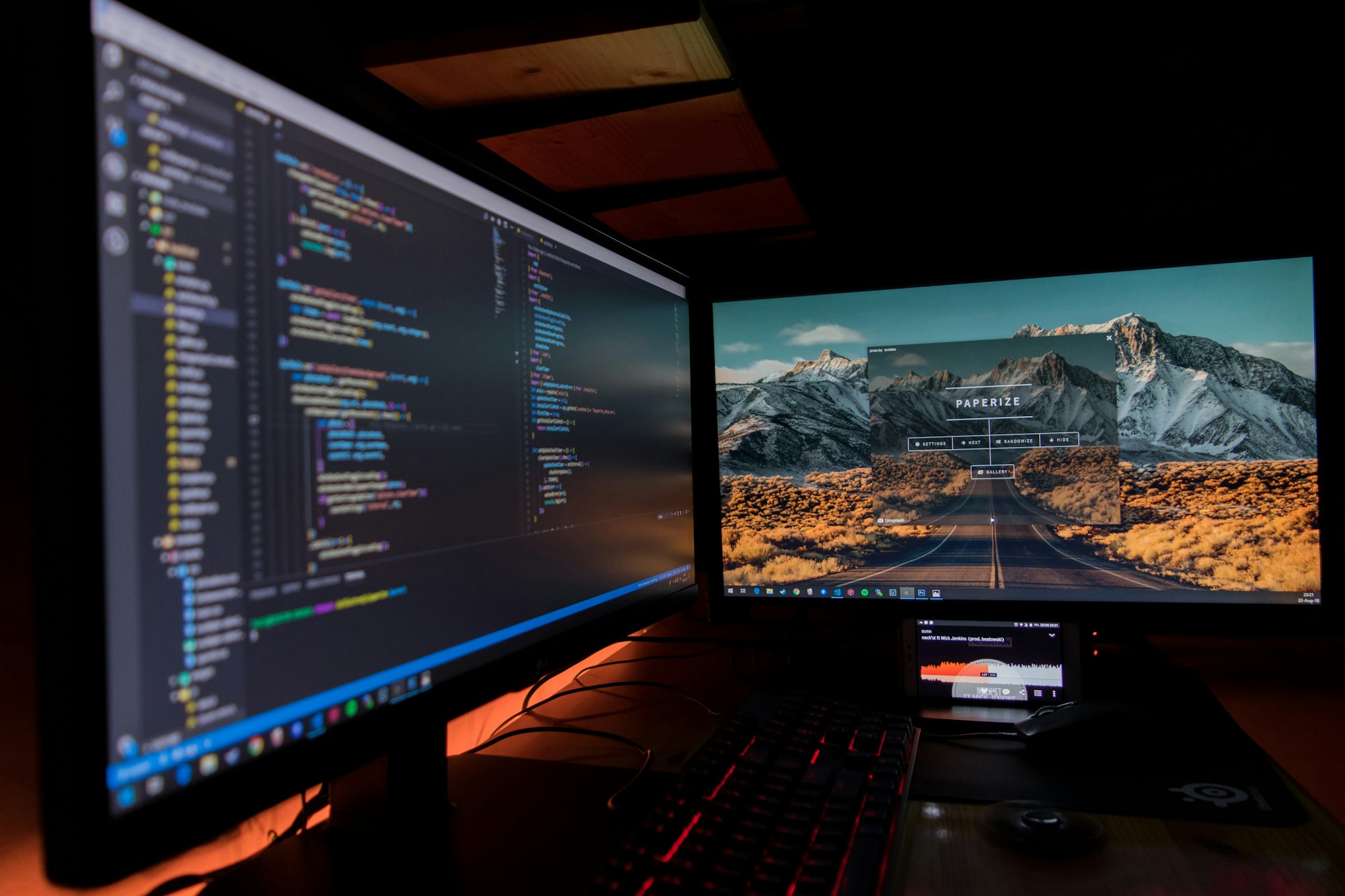 Two monitors side by side in a dark developer workspace, each displaying code, representing the dual signals needed before merging an AI-authored pull request: the diff and the running ephemeral environment